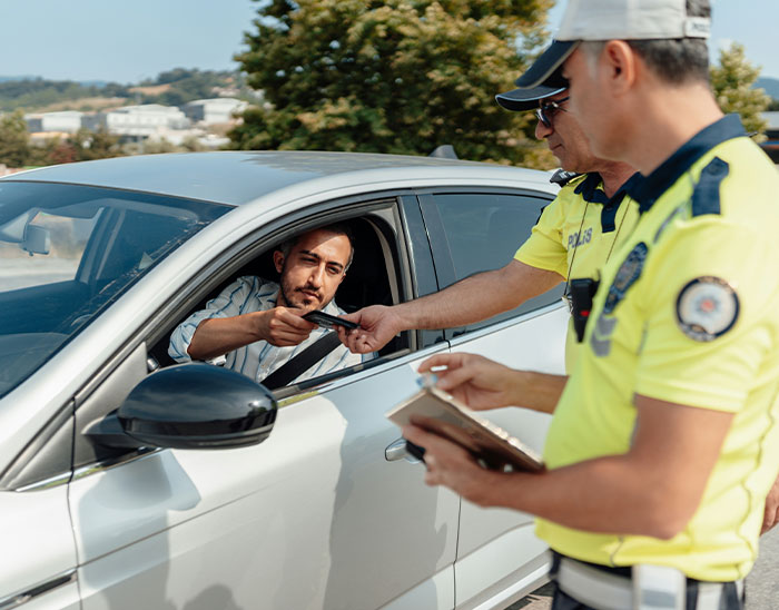 Driver handing license to police officers during a traffic stop, illustrating lawyers and winning case challenges.