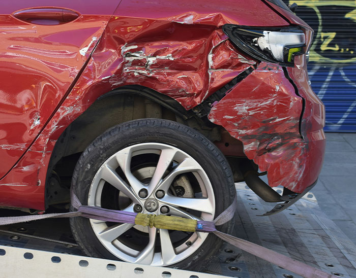 Damaged red car with crumpled rear side and tire strapped on a tow truck after an accident, lawyers assess case outcome.