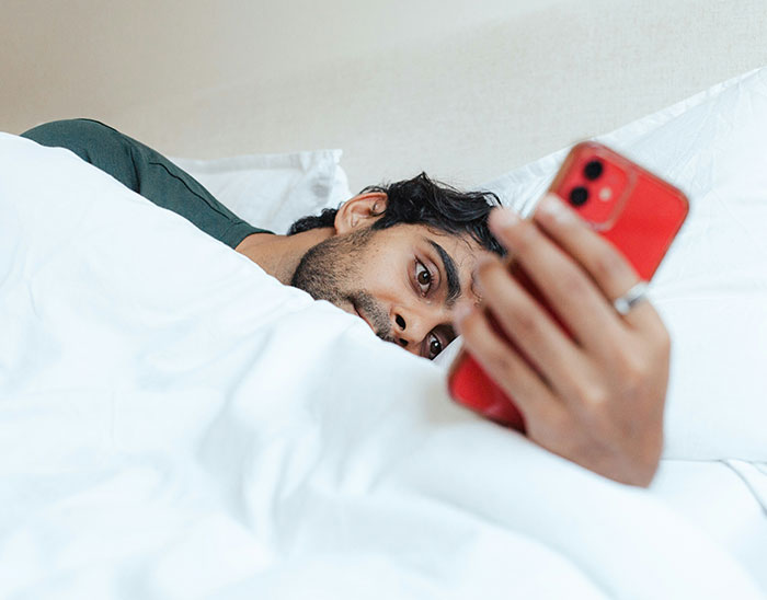 Man lying in bed holding a red smartphone, showing lawyers immediately knew these people are not winning their case.