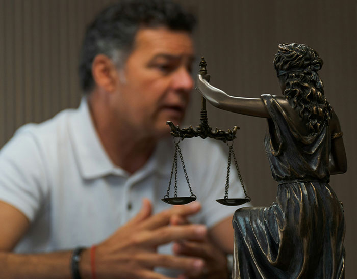 Man speaking with a statue of Lady Justice holding scales, illustrating lawyers and legal case discussions.