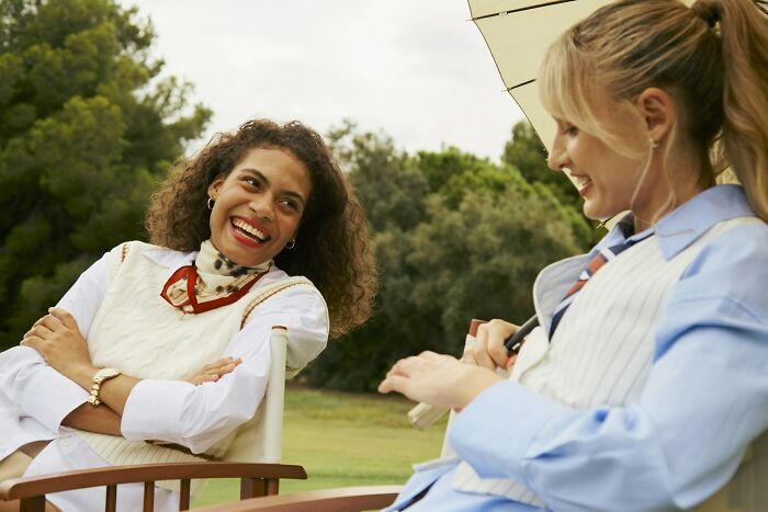 Two women relaxing outdoors at a private resort, smiling and chatting under a sun umbrella on a sunny day.