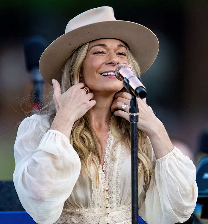 LeAnn Rimes performing live, smiling and adjusting her hair while singing on stage with a microphone in front of her. LeAnn Rimes performing live, smiling and adjusting her hair while singing on stage with a microphone in front of her.