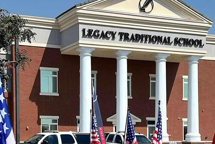 Legacy Traditional School building exterior with cars and flags, related to 5th grade girls revenge plot at school. Legacy Traditional School building exterior with cars and flags, related to 5th grade girls revenge plot at school.