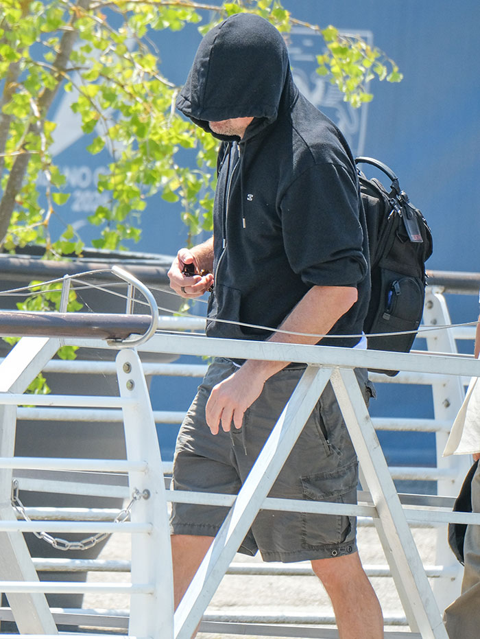 Man wearing a black hoodie and shorts walking outside, showing a strung-out celebrity look after weekend partying event