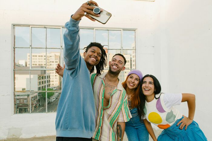 Group of friends smiling and taking a selfie, illustrating social interaction and subtle signs of low self-esteem.