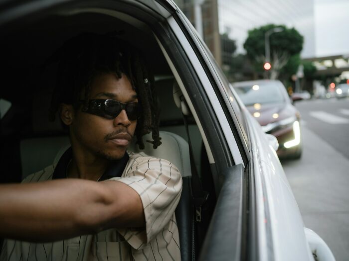 Man wearing sunglasses looking out from car window on a busy street, part of 80 people sharing things others don't know.