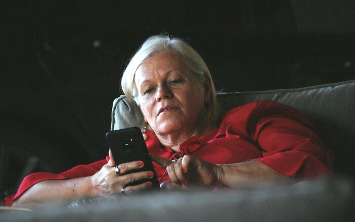 Older woman in a red blouse lying on a couch, looking at her phone, depicting revenge on cheating exes.