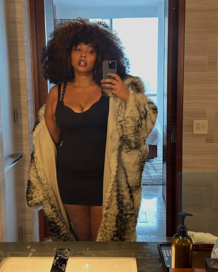 Lizzo taking a mirror selfie wearing a black dress and fur coat, addressing rumored Ozempic use and weight loss method.