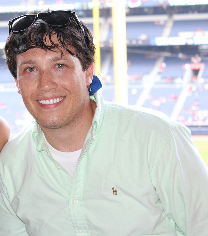 Man smiling in a light green shirt at a sports stadium, related to chiropractor neck pain and locked-in syndrome story.
