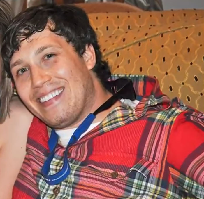 Smiling man in a red plaid shirt sitting, related to chiropractor visit and locked-in syndrome after neck pain treatment.