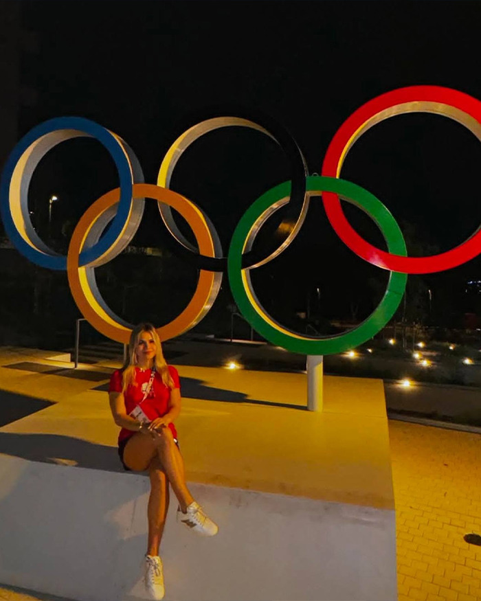 Swimmer sitting near illuminated Olympic rings at night, symbolizing Olympic Village and athlete controversy. Swimmer sitting near illuminated Olympic rings at night, symbolizing Olympic Village and athlete controversy.