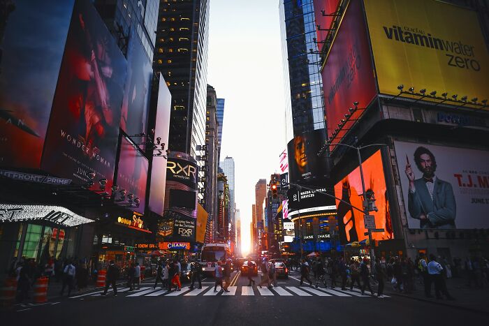 Busy city street at sunset with crowds and large digital billboards, illustrating travel destinations tourists often warn to avoid.