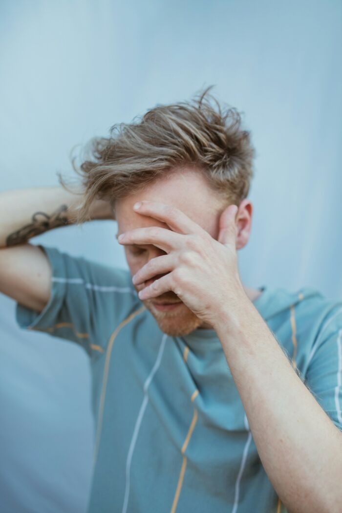 Young man in a casual shirt looking stressed and covering his face, reflecting emotions related to hooking up with a friend’s parent.