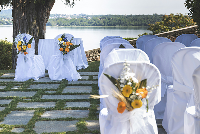 Outdoor wedding seating by a lake with white chair covers and floral decorations, highlighting bride menu drama vegan SIL. Outdoor wedding seating by a lake with white chair covers and floral decorations, highlighting bride menu drama vegan SIL.