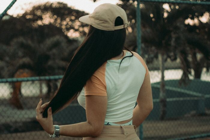Woman wearing a cap, standing outdoors near a fence, reflecting on frustrating experiences with dismissive doctors.