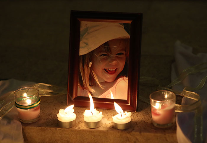Framed photo of a smiling young girl surrounded by lit candles at a memorial for Madeleine McCann.