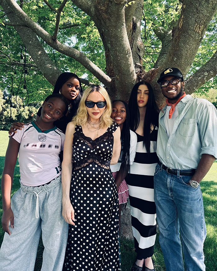 Madonna in a black polka dot dress and sunglasses posing with diverse group outdoors for Pride Month celebration. Madonna in a black polka dot dress and sunglasses posing with diverse group outdoors for Pride Month celebration.