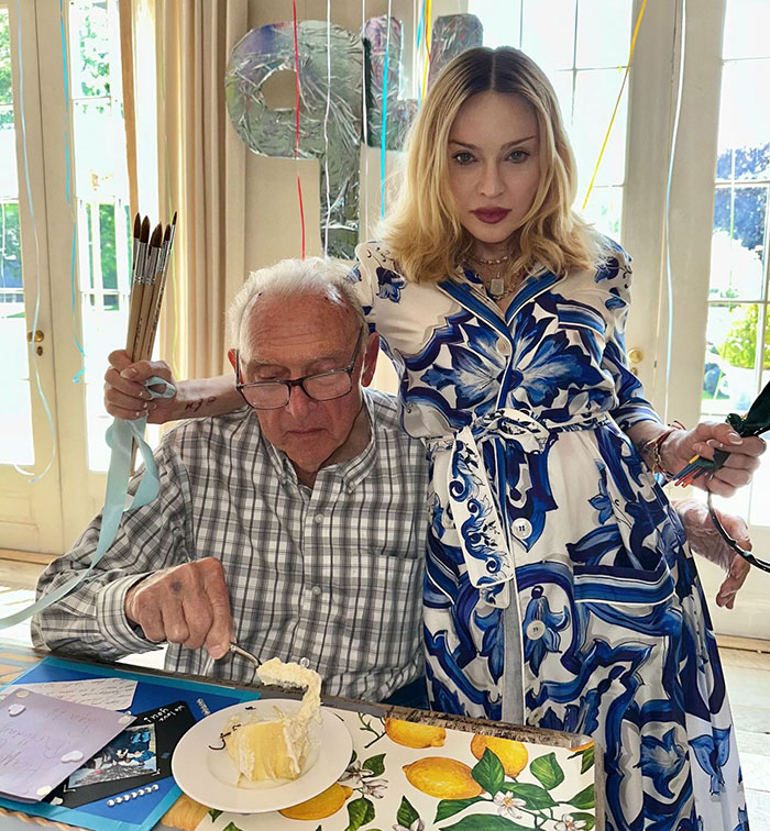 Madonna in a blue floral dress standing by a man eating cake, celebrating Pride Month with paintbrushes and decorations. Madonna in a blue floral dress standing by a man eating cake, celebrating Pride Month with paintbrushes and decorations.