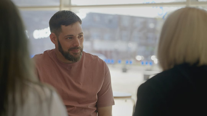 Man with beard in a brown shirt meeting his birth family after being abandoned as a baby in a plastic bag and left in a toilet.