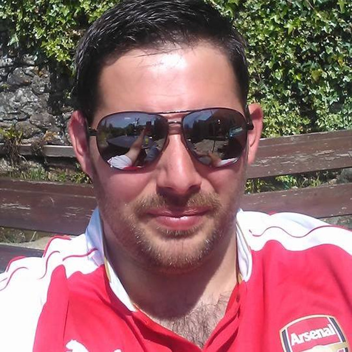 Man wearing sunglasses and red Arsenal jersey sitting outdoors, symbolizing man abandoned as baby meeting birth family after 40 years