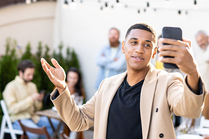 Young influencer marketing coworker takes a selfie confidently at an outdoor office gathering with blurred colleagues in background
