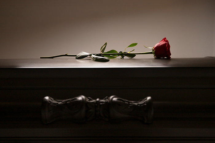 A single red rose rests on a dark wooden coffin symbolizing funeral and prioritizing death over life.