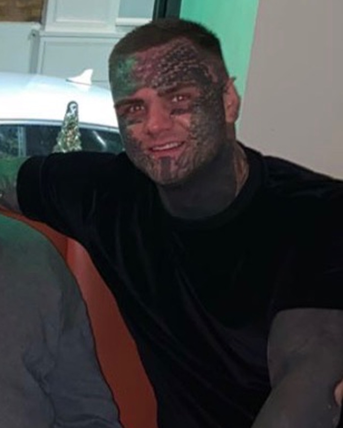 Man with face tattoos smiling indoors, wearing a black shirt, representing immigration and tattooed individual topics. Man with face tattoos smiling indoors, wearing a black shirt, representing immigration and tattooed individual topics.