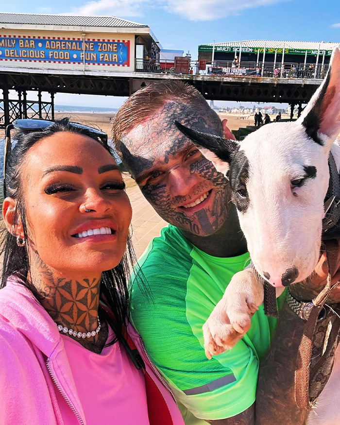 Man with face tattoos smiling outdoors with a woman and a dog near a pier on a sunny day. Man with face tattoos smiling outdoors with a woman and a dog near a pier on a sunny day.