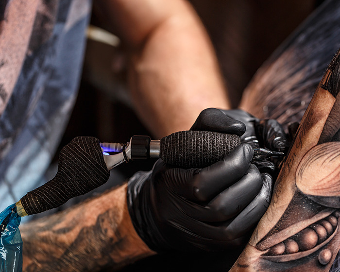 Tattoo artist with black gloves using a machine to create detailed face tattoos on a client's arm. Tattoo artist with black gloves using a machine to create detailed face tattoos on a client's arm.