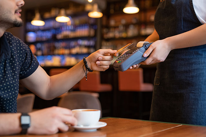 Customer tipping 83 cents while paying with a card in a cafe, barista holding a payment terminal in a casual setting.