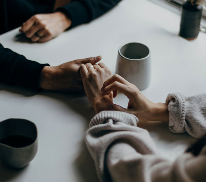 Couple holding hands at a table with coffee cups, illustrating a tense moment in a relationship about splitting 50/50. Couple holding hands at a table with coffee cups, illustrating a tense moment in a relationship about splitting 50/50.