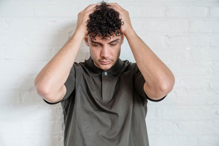 Man with curly hair holding head in frustration, illustrating fiancé worried about woman refusing to wear engagement ring. Man with curly hair holding head in frustration, illustrating fiancé worried about woman refusing to wear engagement ring.
