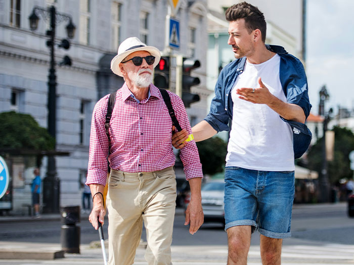 Young man helping elderly man with a cane cross the street, showing kindness that makes him stand out in a rom-com moment