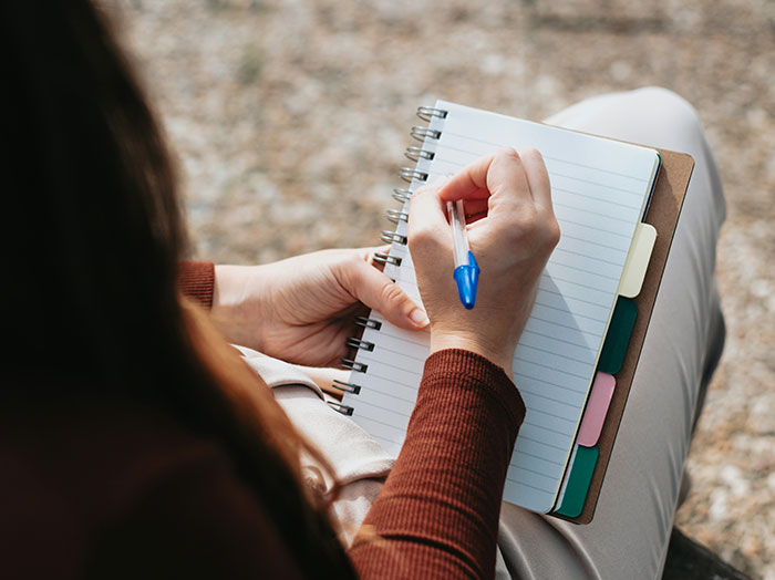 Woman writing in a notebook outdoors, capturing moments when men made women think wow, he stands out in romance.