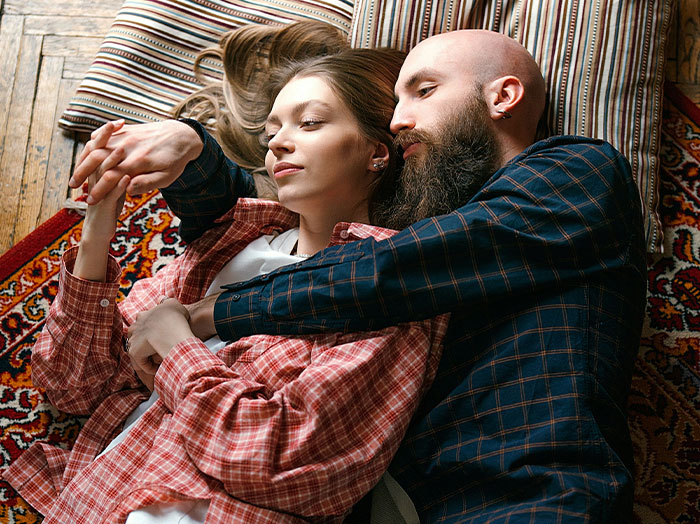 Couple lying on floor rugs, man holding woman close, capturing moments where men made women think wow he stands out.