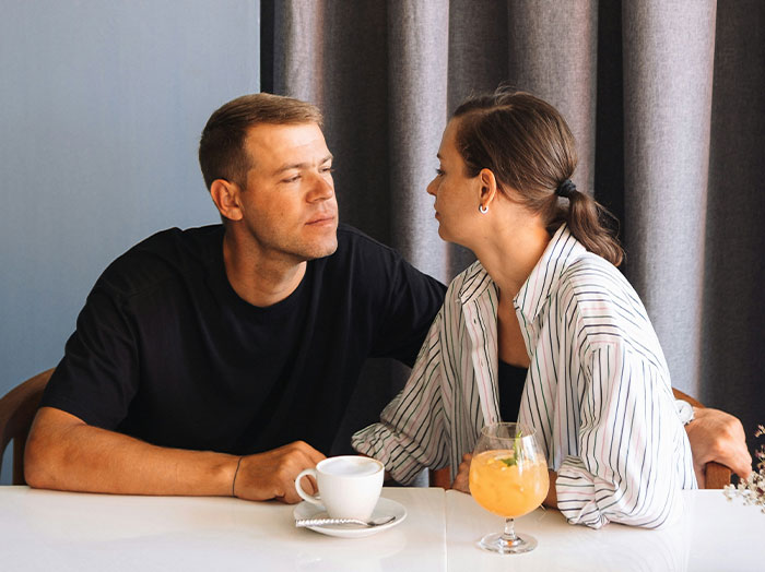 Man and woman sitting closely at a table, sharing an intimate moment that makes him stand out in a romantic setting.