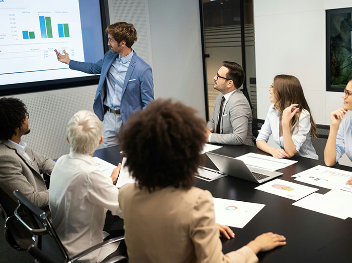 Man in blue blazer giving a presentation to colleagues, showing confidence that made him stand out in the room.