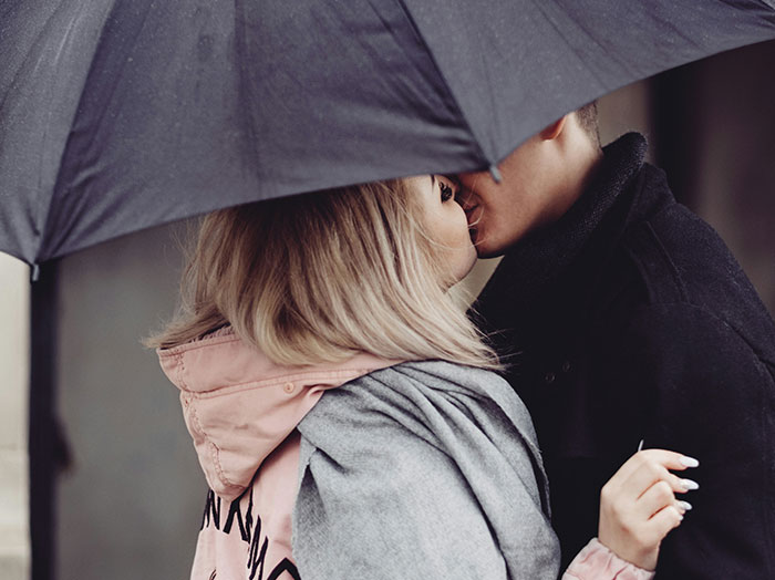 Couple sharing a romantic kiss under an umbrella, capturing a moment that makes men stand out in love stories.