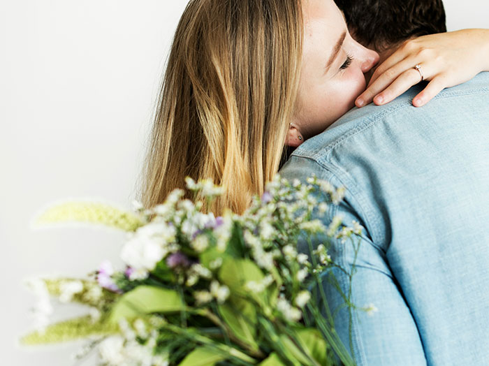 Woman smiling and hugging man while holding flowers, capturing moments where men made women think he stands out.
