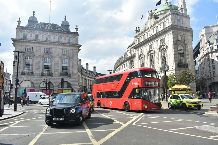 Red double-decker bus and black taxi driving through busy London street, representing honest thoughts about the UK.