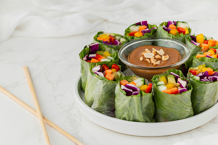 Fresh vegan spring rolls with colorful vegetables served with peanut dipping sauce on a white plate Fresh vegan spring rolls with colorful vegetables served with peanut dipping sauce on a white plate