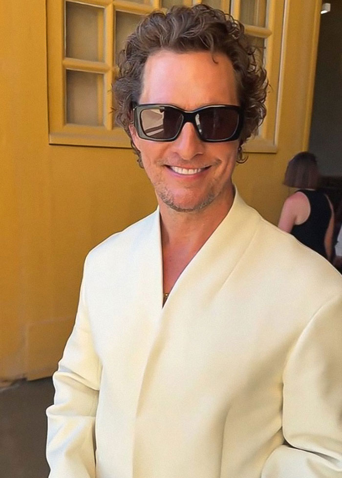Matthew McConaughey wearing sunglasses and a white jacket, smiling indoors with a blurred person in the background Matthew McConaughey wearing sunglasses and a white jacket, smiling indoors with a blurred person in the background