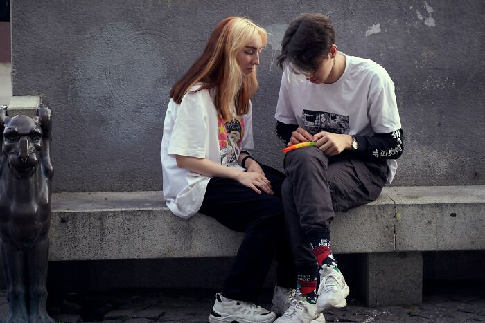 Two young people sitting closely on a concrete bench, illustrating challenges of modern dating experiences.