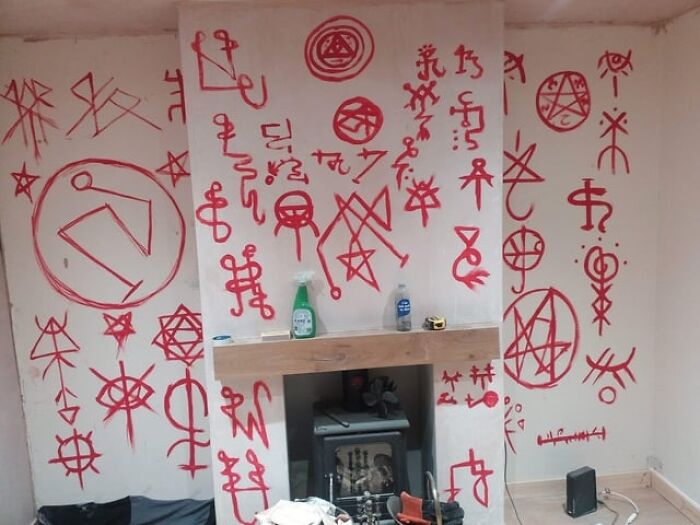 Room with red occult symbols painted on walls above an old fireplace, evoking creepy abandoned explorers’ encounters.