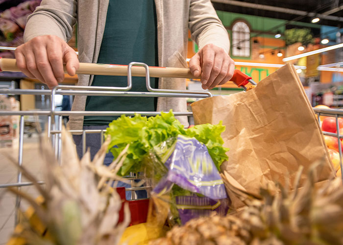 Person pushing a grocery cart with lettuce and paper bags, representing healthy foods to skip eating advice from dentists and doctors.