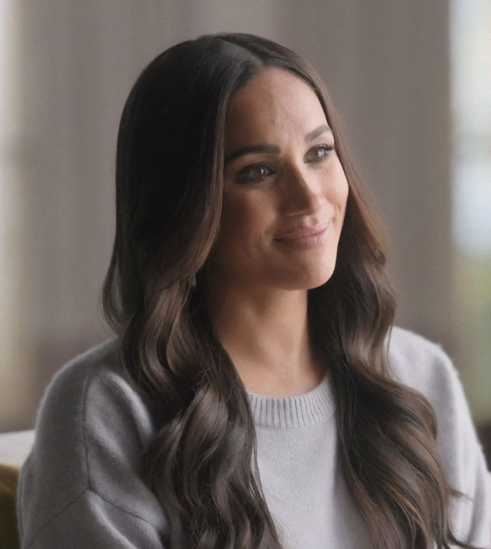 Meghan Markle smiling softly indoors with long wavy hair, linked to twerking pregnancy video and birth conspiracy theory.