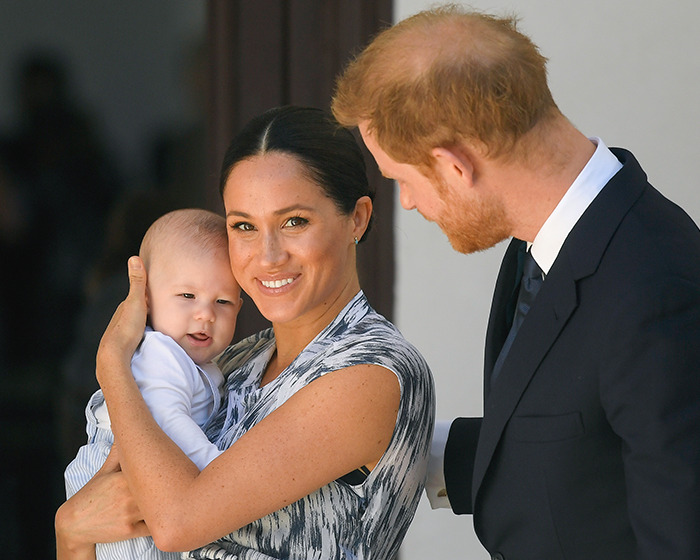 Meghan Markle holding her child while Prince Harry looks on during a public event with family focus.