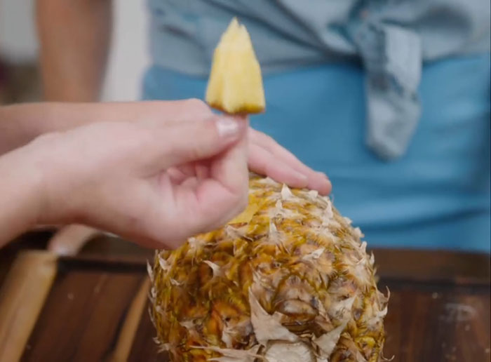 Hand holding a freshly cut pineapple slice over a pineapple, illustrating Meghan Markle kitchen hack concept.