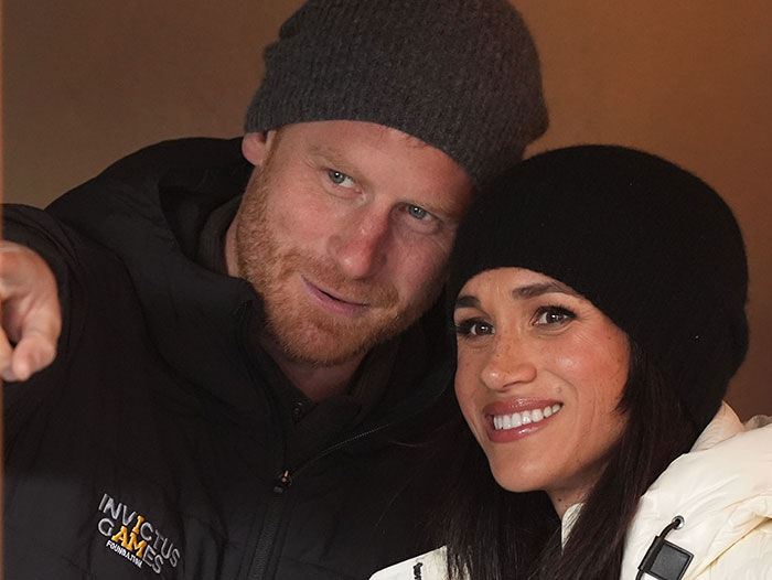 Prince Harry and Meghan Markle wearing winter hats and jackets, smiling and posing closely together.