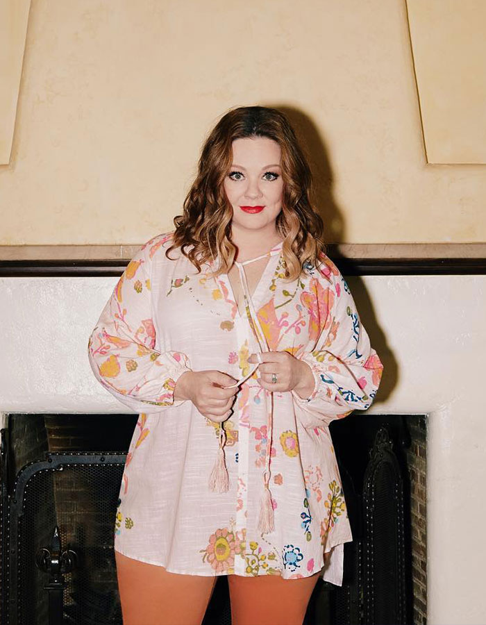 Melissa McCarthy wearing a floral blouse standing indoors, celebrating a major milestone with a rare look-alike daughter pic.